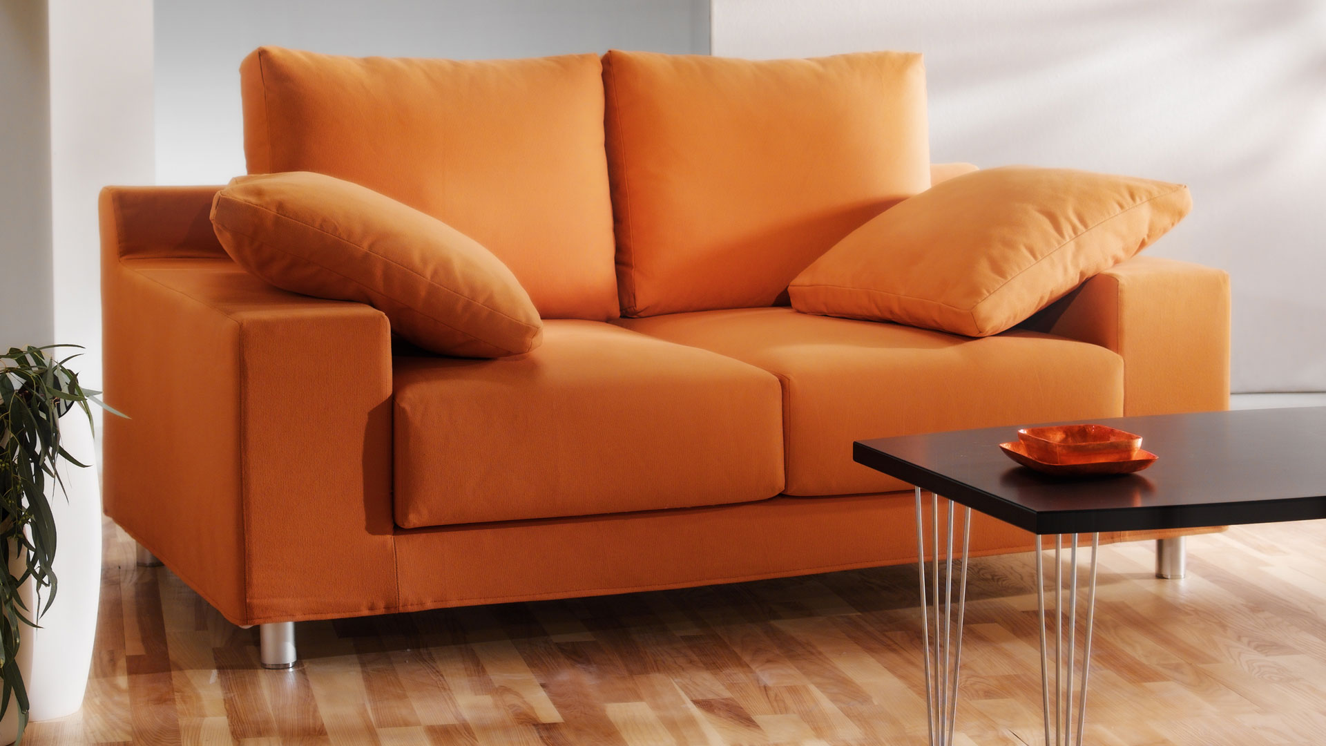 An orange sofa with matching cushions beside a black coffee table