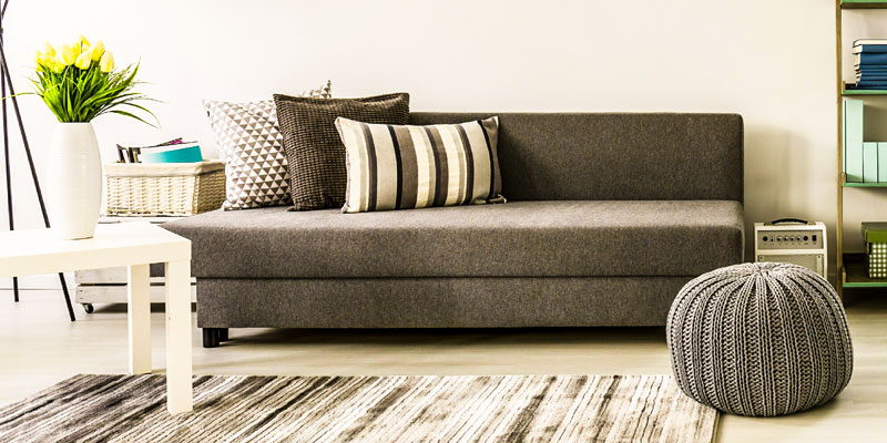 A grey sofa bed with striped cushions and a knitted pouf