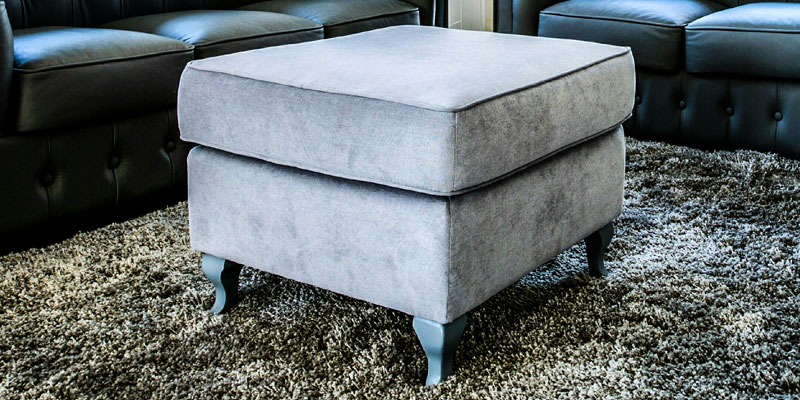 A grey velvet ottoman on a shaggy rug in front of a black sofa