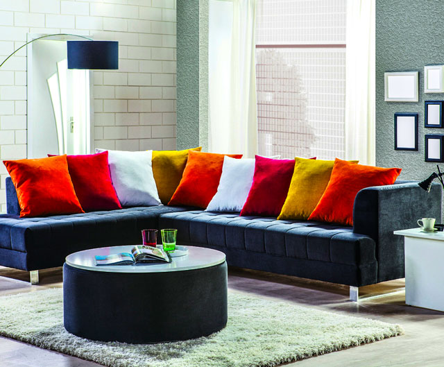 A navy sectional with bright orange, red and yellow cushions and a round coffee table